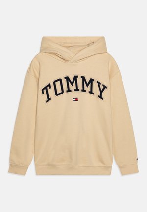 Beiger Hoodie mit Kängurutasche vorne, großem "TOMMY" Schriftzug in Schwarz und gesticktem Logo-Detail am Saum. Weiches Baumwollmaterial.