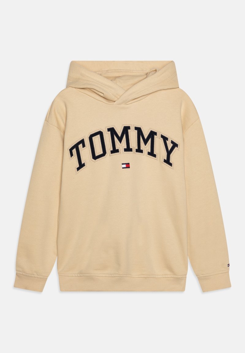 Sweat à capuche beige avec une grande poche kangourou à l'avant, l'inscription "TOMMY" en noir, et un détail de logo brodé à l'ourlet. Matière en coton doux.