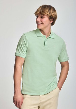 Camisa polo verde claro con collar clásico, mangas cortas y logo bordado sutil en el pecho. Material de algodón con una textura suave.