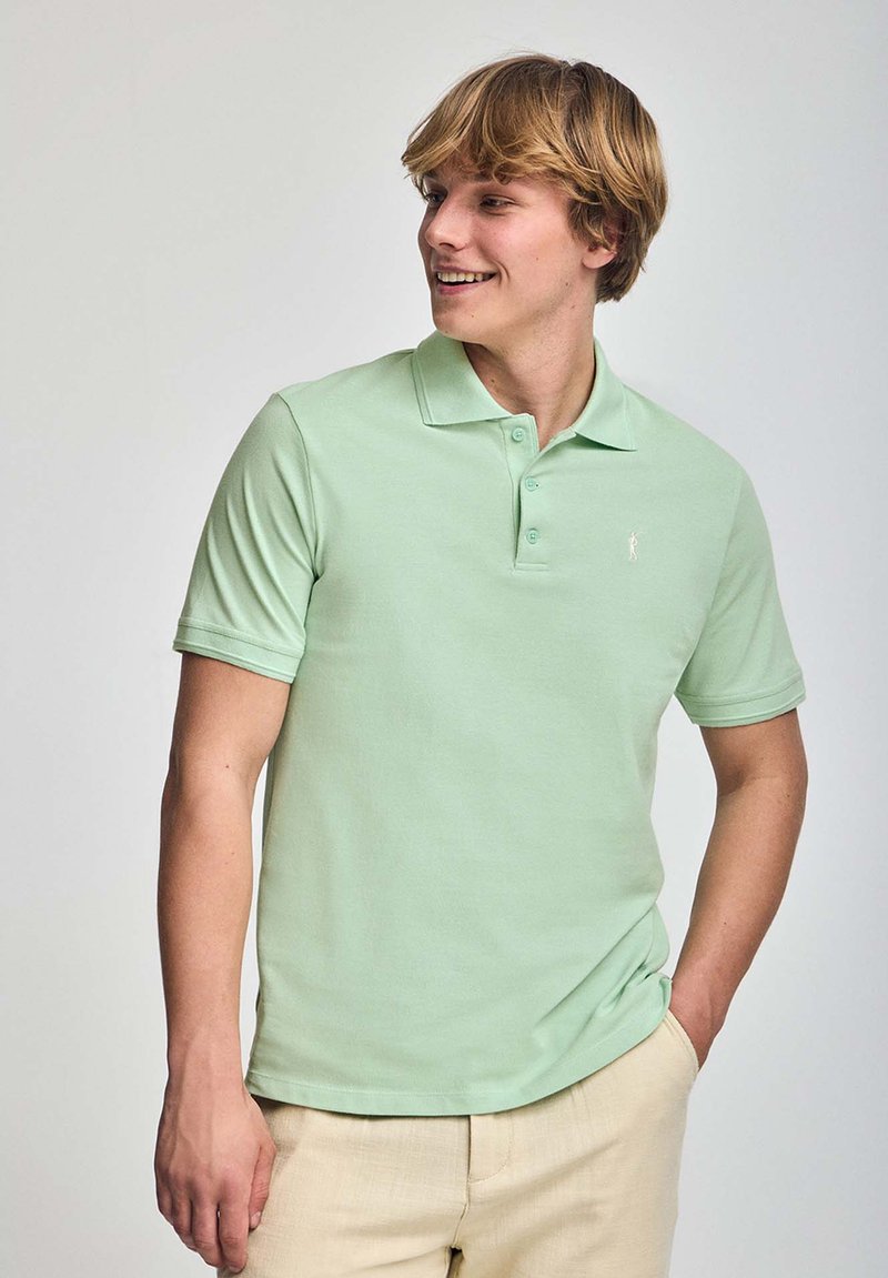 Ljusgrön pikétröja med klassisk krage, korta ärmar och subtilt broderad logotyp på bröstet. Tillverkad av bomull med en mjuk textur.