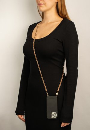 Black phone case with a gold chain strap worn across the body, displaying the phone's camera cutout and a smooth matte finish.