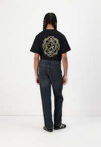Black cotton t-shirt with yellow geometric graphic on back, paired with dark blue denim jeans and black footwear with white stripes.