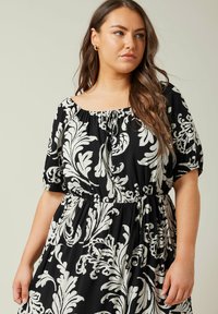 Vestido de estampado floral en blanco y negro con mangas abullonadas, cintura fruncida y escote cuadrado. Tela ligera con una textura suave.