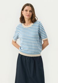 Randig stickad kortärmad tröja i ljusbeige och blå. Har en rundad halsringning och ribbad nederkant. Bärs med en mörk kjol.