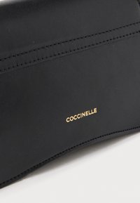 Oggetto in pelle nera con dettaglio di doppia cucitura e nome del marchio "COCCINELLE" impresso in oro sulla superficie.