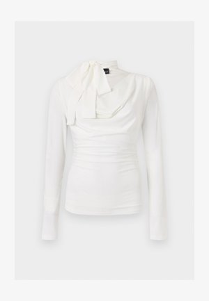 Valge, keha järgnev pikkade varrukatega pluus, millel on drapeeritud lõige ja vasakul pool seotud lips.