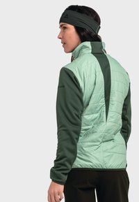 Grüne und mintfarbene Pufferjacke mit strukturiertem Vorderteil, glatten Ärmeln, hohem Kragen und kontrastierendem Rückenteil; getragen mit einem passenden Haarband.