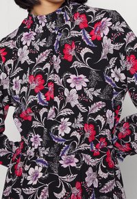 Černá látka s květinovým vzorem, který obsahuje červené, fialové a bílé květiny. Vysoký límec s nařasením a elastický pas.