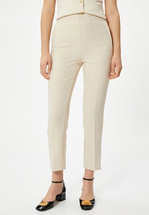 Beige tailored trousers with a high waist, straight legs, and subtle pinstripes, paired with black and yellow block-heeled shoes.