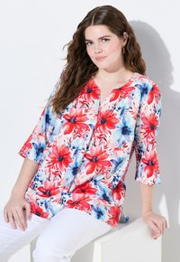 Blommig topp med röda och blå blommor på en vit bakgrund, med V-ringning, 3/4-långa ärmar och en avslappnad passform.