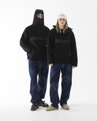 Felpe in pile nere con colli alti e zip, indossate su denim scuro con una stampa sottile. Gli accessori includono un cappellino e vari tipi di scarpe.