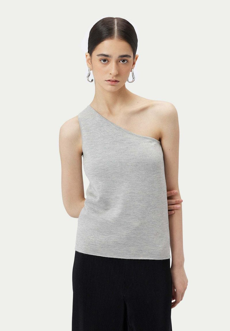 Grå enaxlad topp i mjukt tyg, med en figurnära design. Modellen bär den med svarta plisserade byxor.