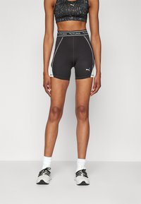 Pantaloni athletic neri a vita alta con accenti bianchi ai lati, realizzati in un tessuto elasticizzato e con una vita con marchio. Indossati con scarpe da ginnastica nere e bianche.