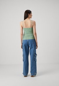Green and blue patterned tank top with thin straps, paired with light blue cargo pants featuring side pockets and a loose fit.