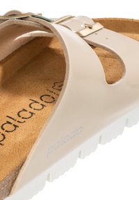 Beige sandaal met een glanzende afwerking, verstelbare zilveren gesp en een gevoerde kurken inlegzool. Witte rubberen zool met een gestructureerd grippatroon.
