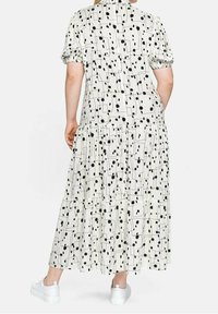Weißes, geschichtetes Maxikleid mit schwarzem geometrischem und gepunktetem Muster, kurzen Puffärmeln und lockerer Passform. Kombiniert mit weißen Turnschuhen.