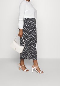 Blusa bianca a maniche lunghe con texture; pantaloni a gamba larga bianco e nero con motivo; borsa bianca; décolleté bianche con tacco a spillo.