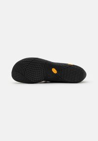Suola di scarpa in gomma nera con superficie texturizzata caratterizzata da un motivo a nido d'ape e un piccolo etichetta di marchio arancione.