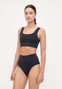 Black cropped tank top with wide straps and smooth, stretchy material; paired with high-waisted bikini bottoms in the same color and texture.