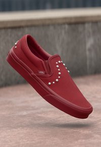 Rote Leinenschlupfschuhe mit weißen Nietenakzenten an der Seite. Sie haben eine abgerundete Schuhspitze und eine strukturierten Gummisohle.