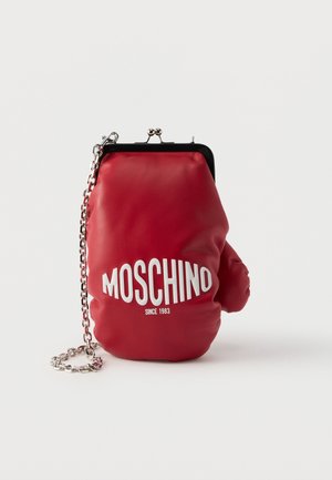 Punane nahast käekott, mis on kujult kui poksikinnas, millel on valgete tähtedega kiri "Moschino Since 1983" ja hõbedane kett rihmana valgel taustal.