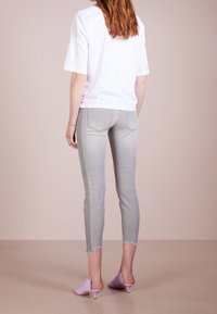 T-shirt bianca a maniche corte, jeans skinny grigi con orli sfrangiati, e sabot color lavanda con punta aperta. Look semplice e casual con tessuti morbidi.