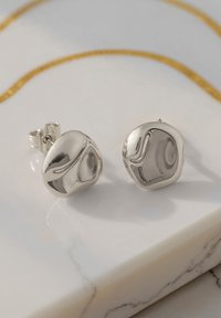 Orecchini a bottone in argento con una forma liscia e organica e dettagli a onde sottili. La finitura lucida esalta la texture riflettente.