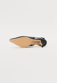 Svart stiletthæl sko med spiss tå og glatt skinnoverdel, en liten stropp og en beige såle med horisontale stripeaksenter.