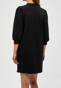 Robe sweat-shirt noire avec manches bouffantes, encolure arrondie et texture lisse. Longueur au-dessus du genou avec poignets côtelés.