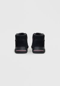 Zapatos altos de ante negro con un acolchado en el collar, que presentan sutiles acentos rojos y una suela de goma texturizada.
