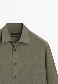 Koszula zapinana na guziki w oliwkowej zieleni, wykonana z teksturowanej tkaniny, z klasycznym kołnierzykiem i czarnymi guzikami. Metka wskazuje "Massimo Dutti".