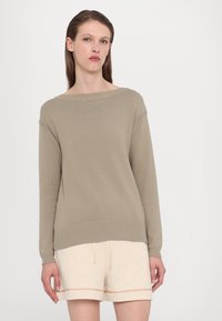 Beige strikket genser med bred hals, ribbestrikkede mansjetter og nederkant. Kombinert med lyse shorts med snøring og kontrasterende søm.
