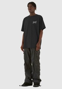 Sort oversized t-shirt med korte ærmer, med hvid grafisk tryk på brystet. Sat sammen med mørke cargo-bukser og sorte sneakers.