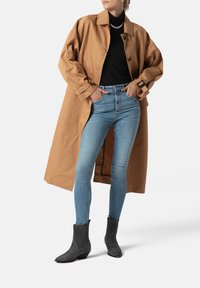 Cotton trench coat in tan, layered over a black turtleneck, paired with light blue jeans and gray ankle boots with a western design.