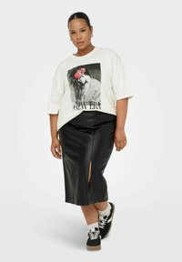 Camiseta gráfica blanca con un estampado en blanco y negro con acentos florales, combinada con una falda midi negra de cuero sintético con una apertura lateral.