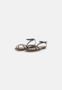 Musthave lamed mustad, mille õhukeste rihmadega, minimalistlik disain, avatud varvas ja paindlik lame tald. Reguleeritav pahkluu rihm on kaasas.