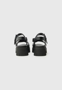 Black platform sandals with a smooth leather upper, featuring two adjustable straps and textured rubber soles embossed with "HUGO."