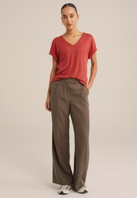 Haut en V texturé rouge avec des manches retroussées, associé à un pantalon large en kaki et des baskets. Design simple et décontracté avec une coupe ample.