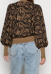 Brun och svart zebramönstrad stickad tröja med puffärmar och ribbade muddar, tillsammans med ljusblå högmidjade denimjeans.