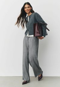 Gray knitted cardigan with wooden buttons over a white top, paired with gray pleated trousers and burgundy patent leather bag and shoes.