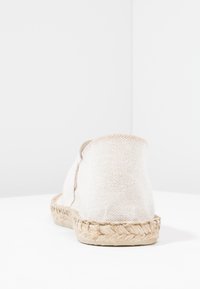 Beige espadrille shoe made of woven fabric, featuring a rope sole and a round, open back without a heel.