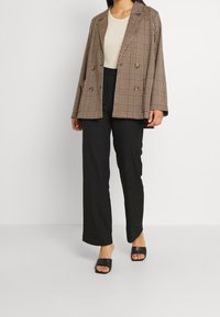 Dubbelknäppt rutigt blazer i brunt och beige, avslappnad passform, med två framfickor. Bärs över en ljus topp och matchas med svarta byxor och slidesandaler.