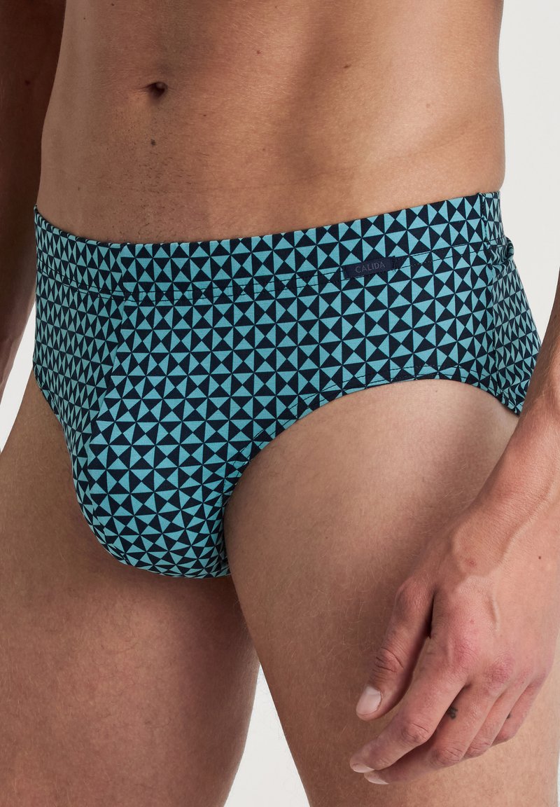 Zwemslip met een geometrisch patroon van lichtblauwe driehoeken op een donkerblauwe achtergrond, gemaakt van rekbare stof. Voorzien van een Calida-label.