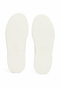 Semelles de baskets blanches en caoutchouc texturé. Elles présentent une empreinte de logo discrète et une forme arrondie et lisse avec des bords nets.