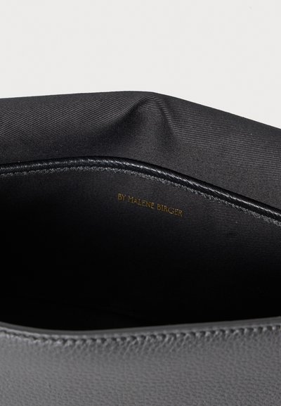 Εσωτερικό μαύρης δερμάτινης τσάντας χειρός με λεία επένδυση από ύφασμα, διακριτική λάμψη και το όνομα της μάρκας "BY MALENE BIRGER" σε ανάγλυφο χρυσό.