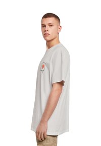 Grå bomulds-t-shirt med korte ærmer, der har et lille rødt og sort grafikdesign på venstre brystområde. Skræddersyet pasform.