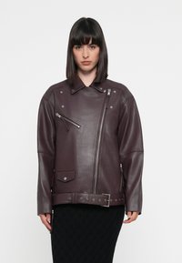 Veste en cuir bordeaux de style motard avec une fermeture éclair diagonale, des accessoires en argent, une poche poitrine et un détail de ceinture à l'ourlet. Texture lisse et coupe oversize.
