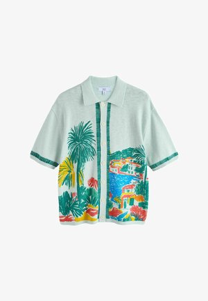 Short-sleeve button-up shirt with collar, featuring colorful tropical landscape print of palm trees, water, and buildings on light green fabric.