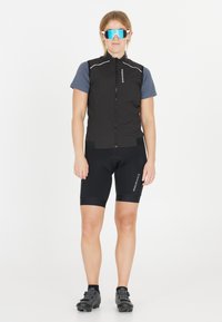 Sort cykelvest med lynlås foran, parret med sorte shorts med polstret sæde. Blå reflekterende solbriller fuldender outfittet.