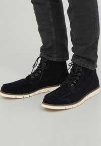 Botas de tobillo de ante navy con suelas de goma blanca en contraste, seis ojales para los cordones y un diseño de punta plana. Acabado texturizado con costuras visibles.